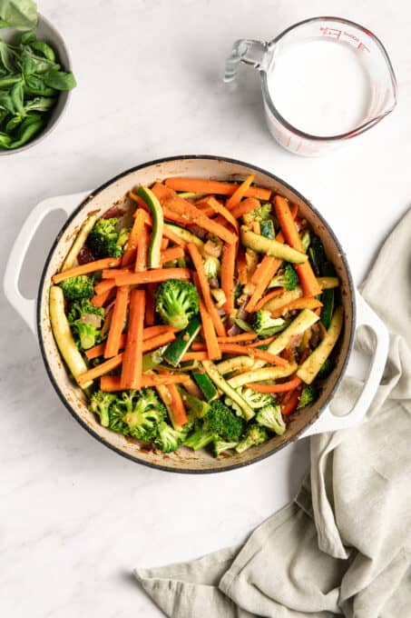 Carrots, zucchini, broccoli, and more cooking in a pan.