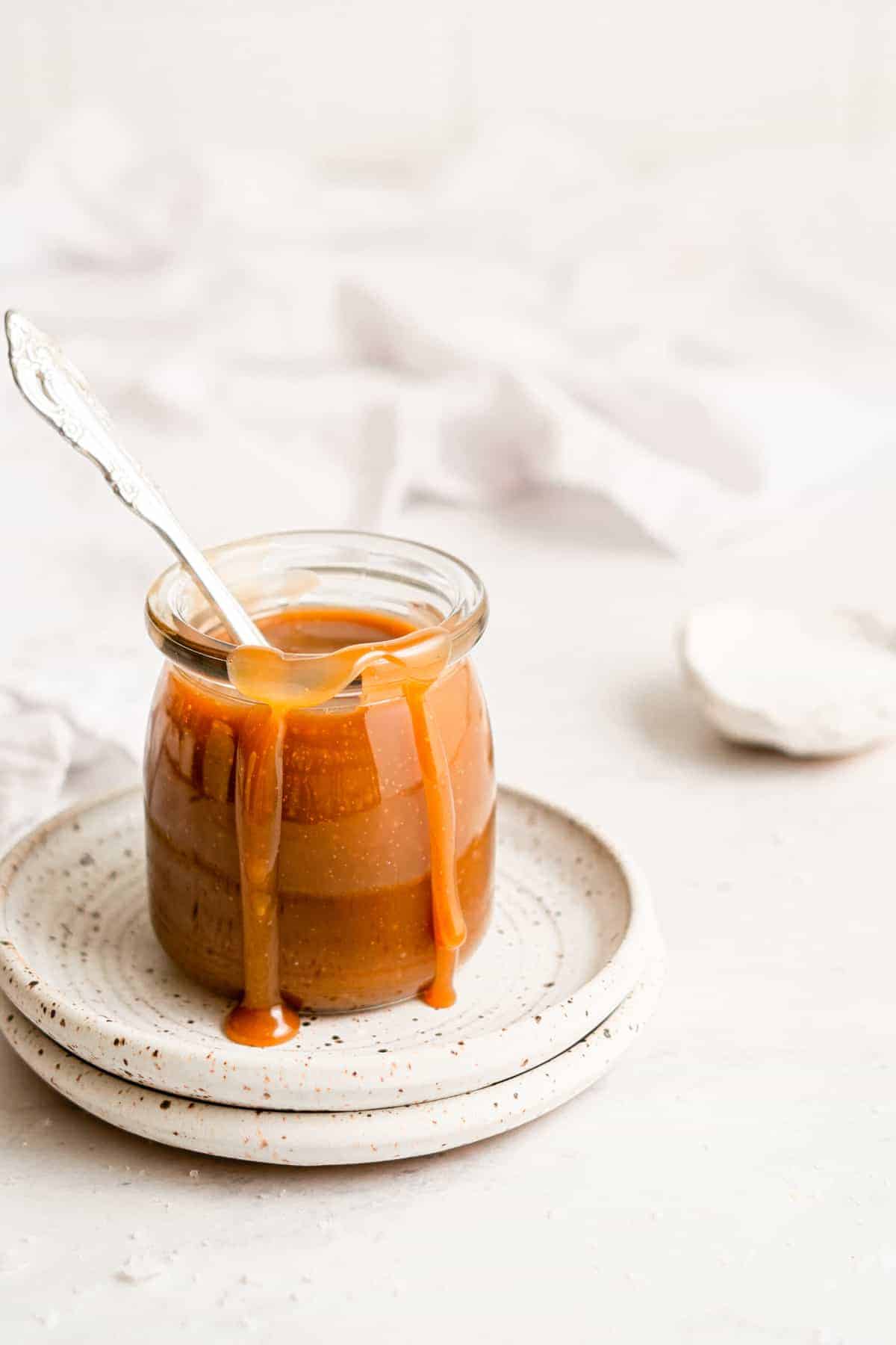 Vegan caramel sauce in a jar, with some caramel dripping down the side.