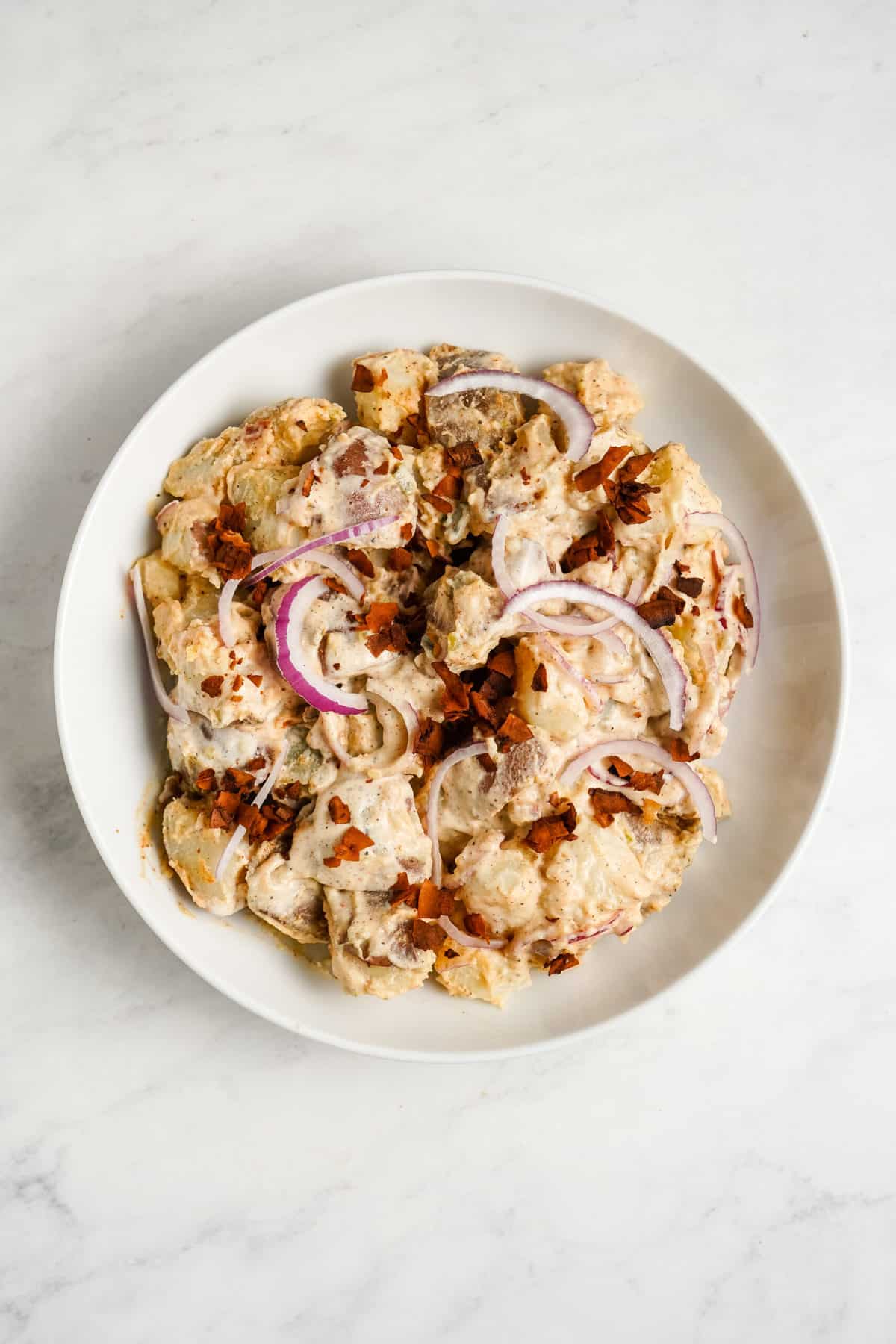 A plate of creamy potato salad with red onions.