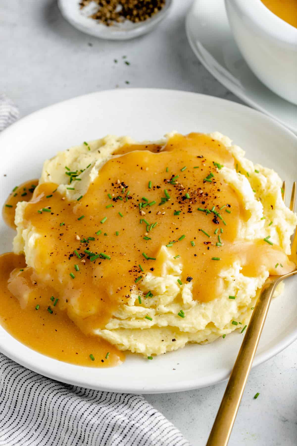 Mashed potatoes on white plate, covered with gravy and topped with minced herbs