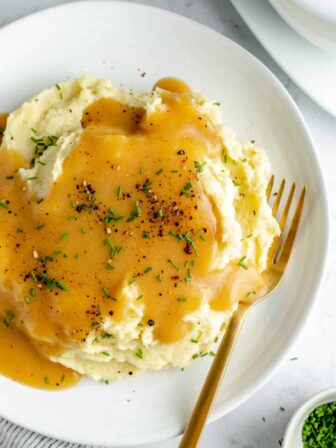 Overhead shot of mashed potatoes on white plate topped with gravy
