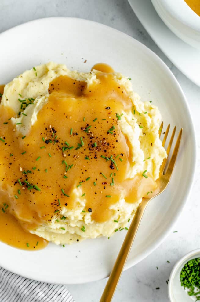 Overhead shot of mashed potatoes on white plate topped with gravy