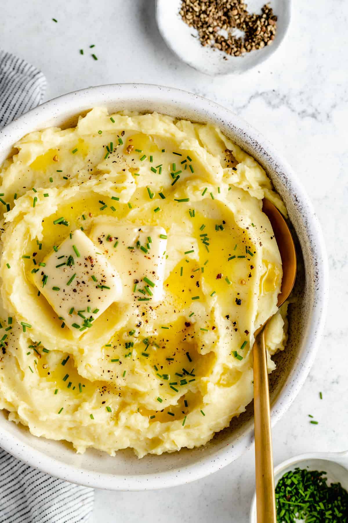Overhead shot of mashed potatoes in bowl topped with pats of butter and herbs