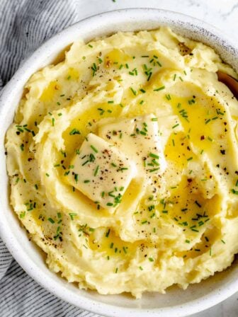 Overhead shot of Vegan Mashed Potatoes in bowl topped with two pats of butter and minced herbs