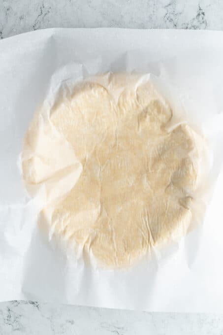 A rolled out pie crust covered with parchment paper.