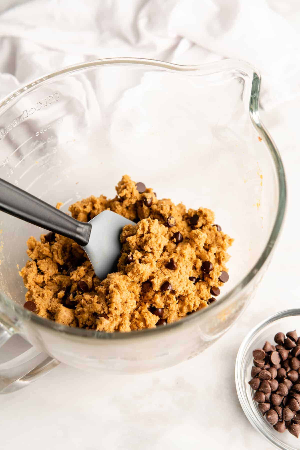 Cookie dough being mixed in glass bowl with spatula