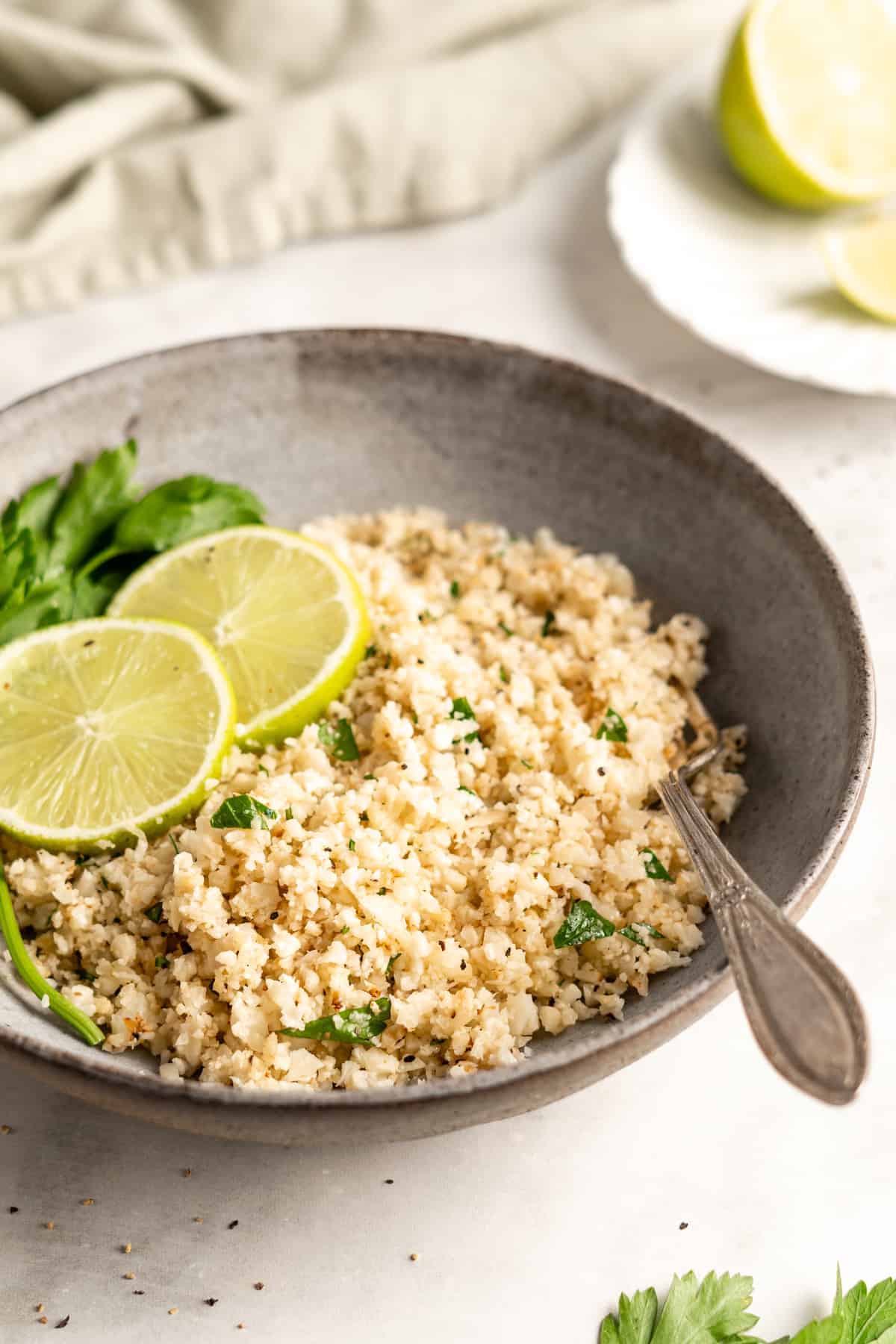 Cauliflower rice in bowl with fork, garnished with lime slices and parsley