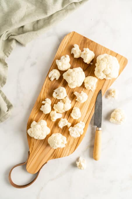 Overhead view of cauliflower florets on wooden cutting board with knife