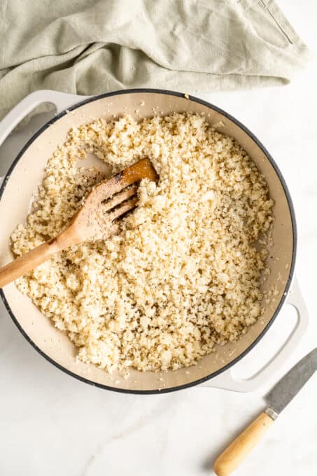 Overhead view of cooked cauliflower rice in cast iron skillet with wooden spatula
