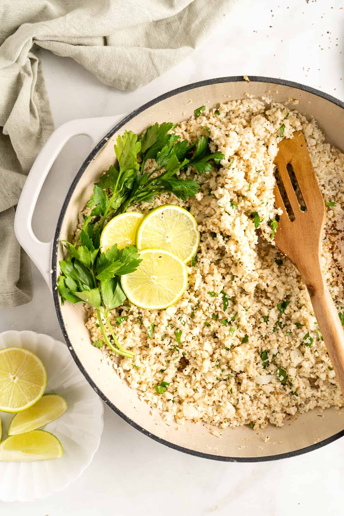 Overhead view of cauliflower rice in skillet garnished with parsley sprigs and lime slices