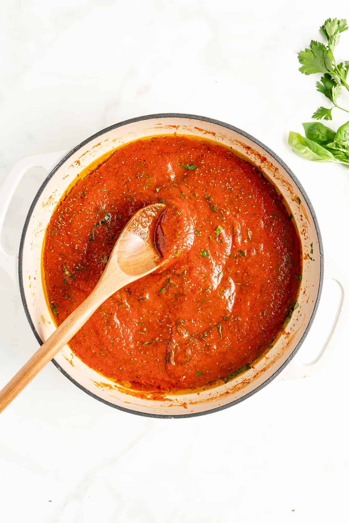 Overhead view of homemade marinara sauce in white pot with wooden spoon
