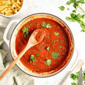 Overhead view of homemade marinara sauce in pot with parsley leaves scattered on top