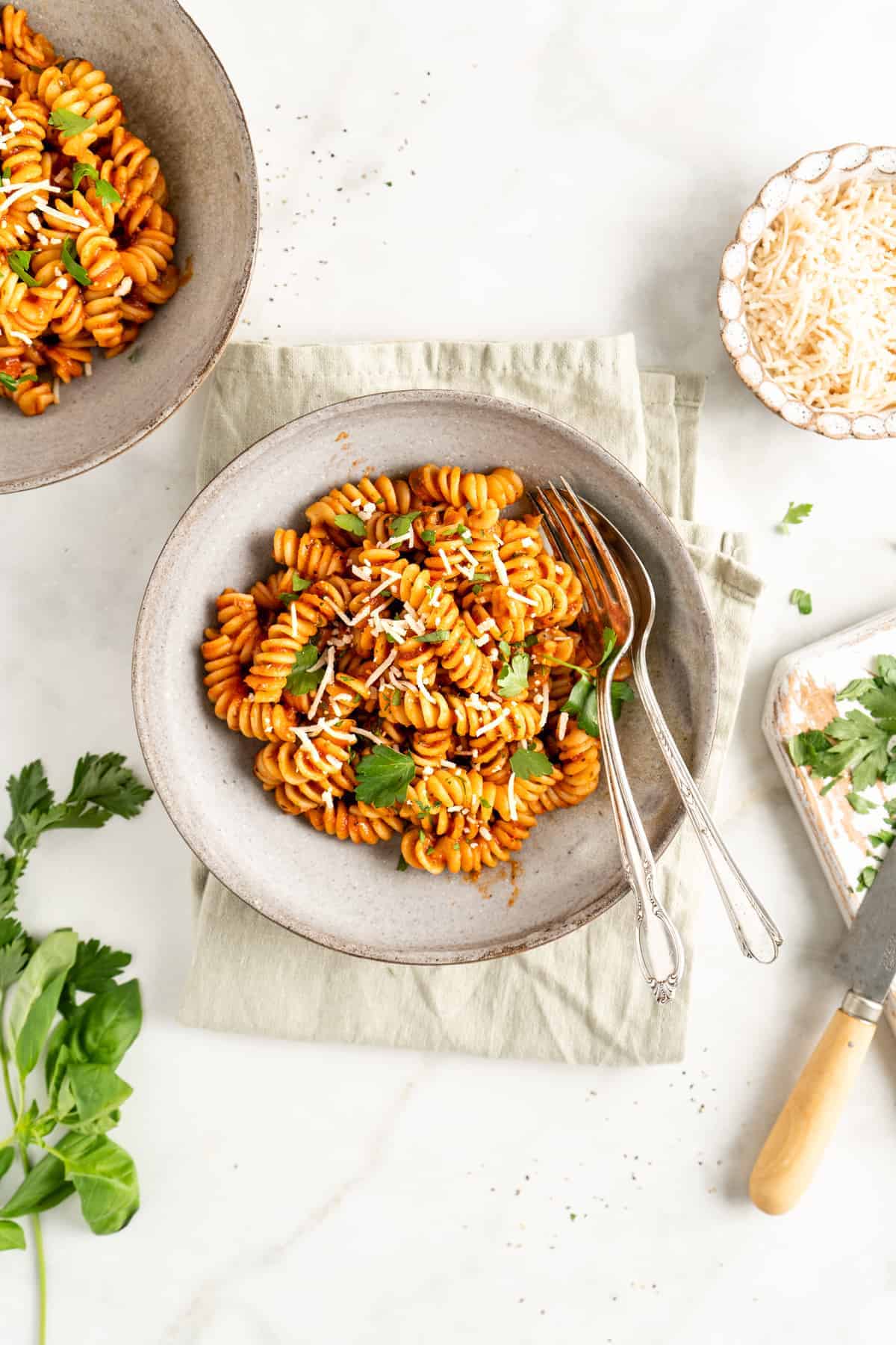 Overhead view of 2 bowls of rotini with marinara, with parmesan and parsley leaves for garnish