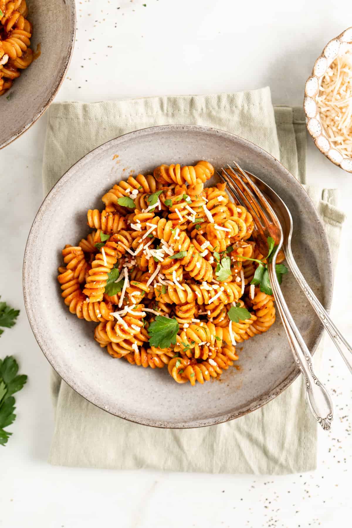 Bowl of rotini in marinara sauce with parmesan and parsley garnishes