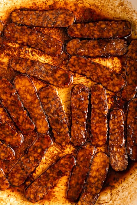 Closeup of tempeh bacon slices being cooked