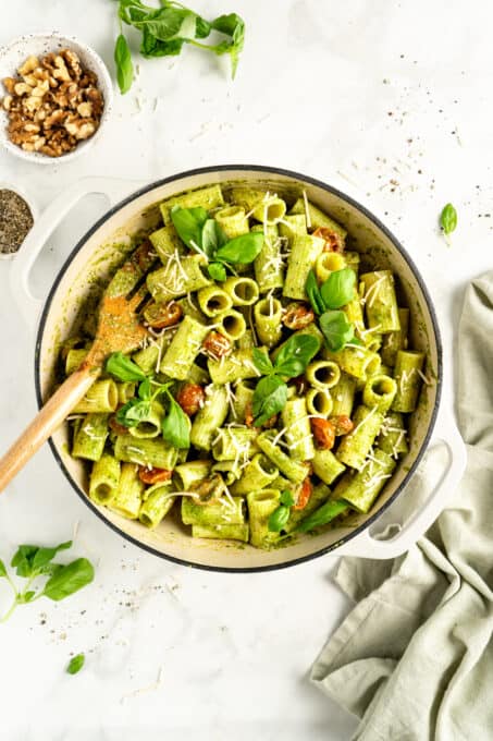 Overhead view of pesto pasta in bowl with wooden spatula and small bowl of nuts