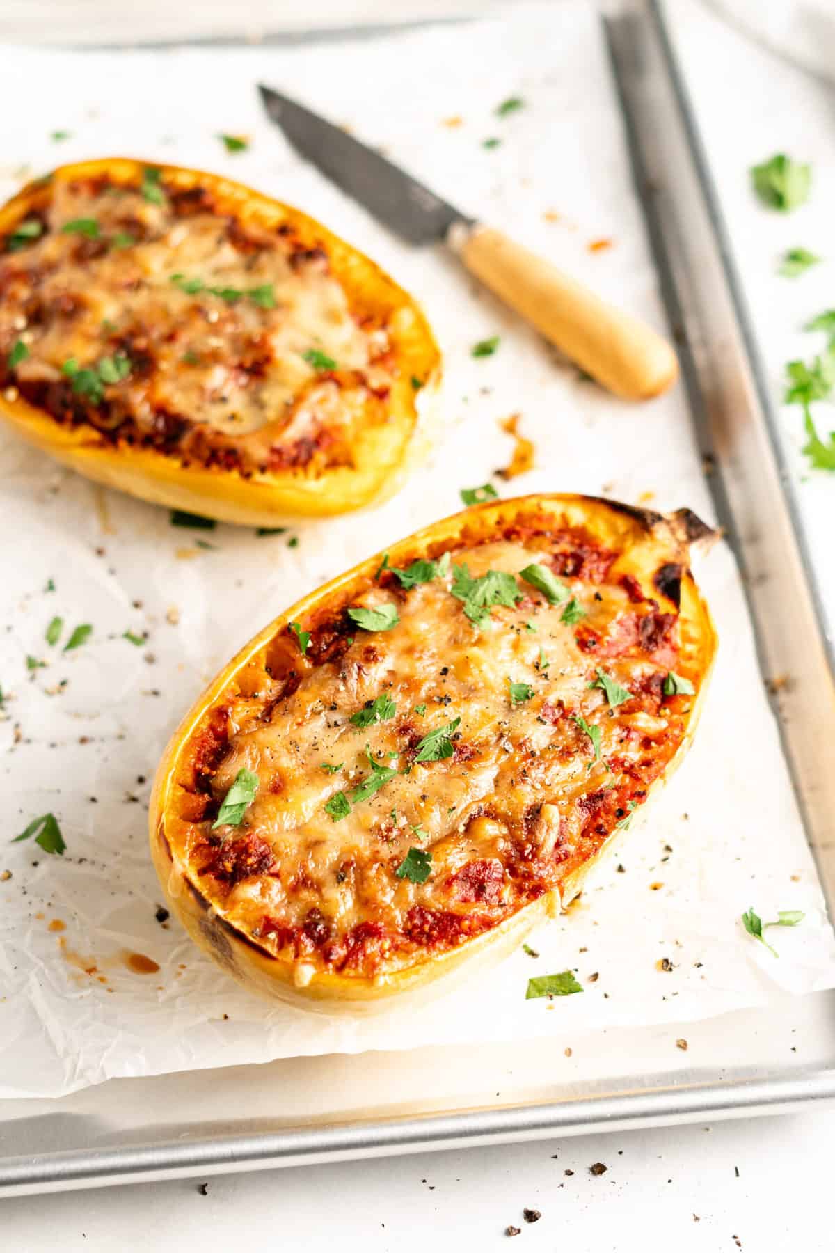 Two lasagna-stuffed spaghetti squash halves on parchment-lined baking sheet