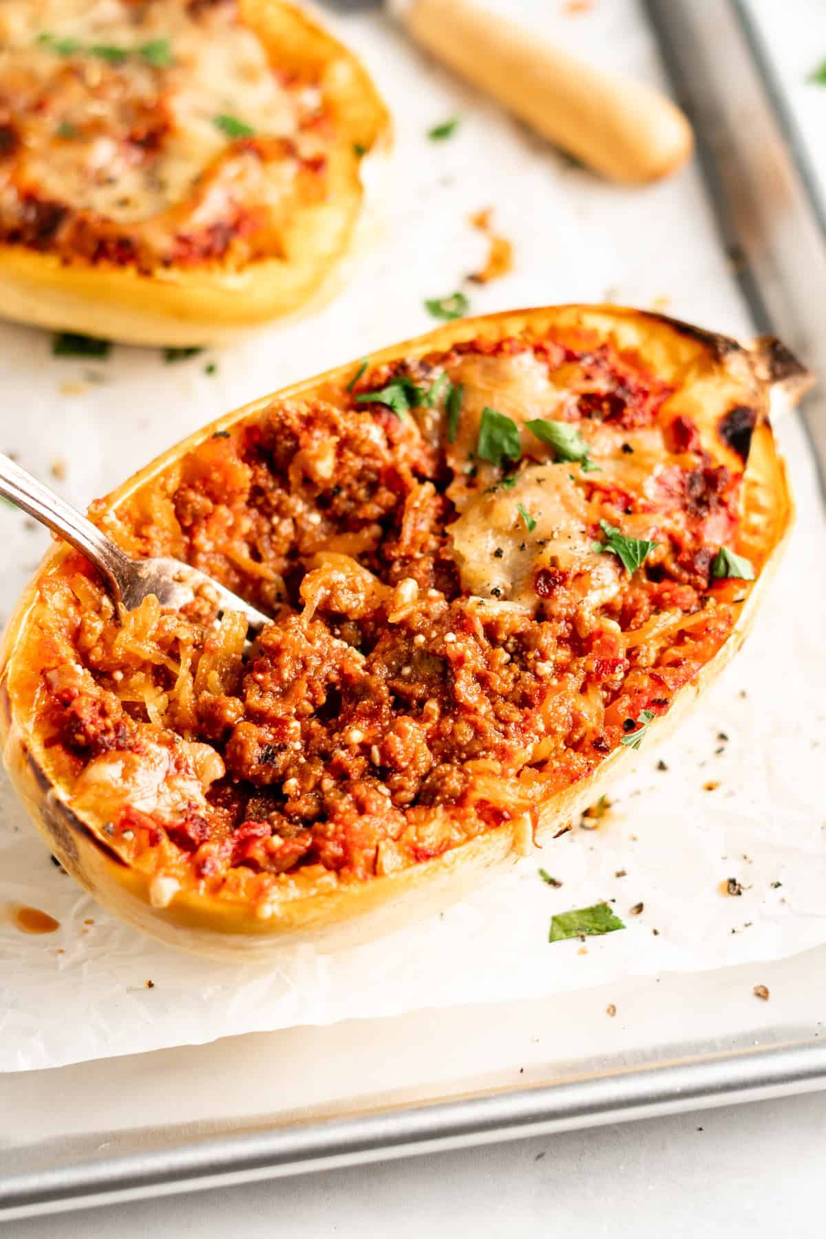 Spaghetti squash lasagna boat on parchment lined baking sheet with fork inside
