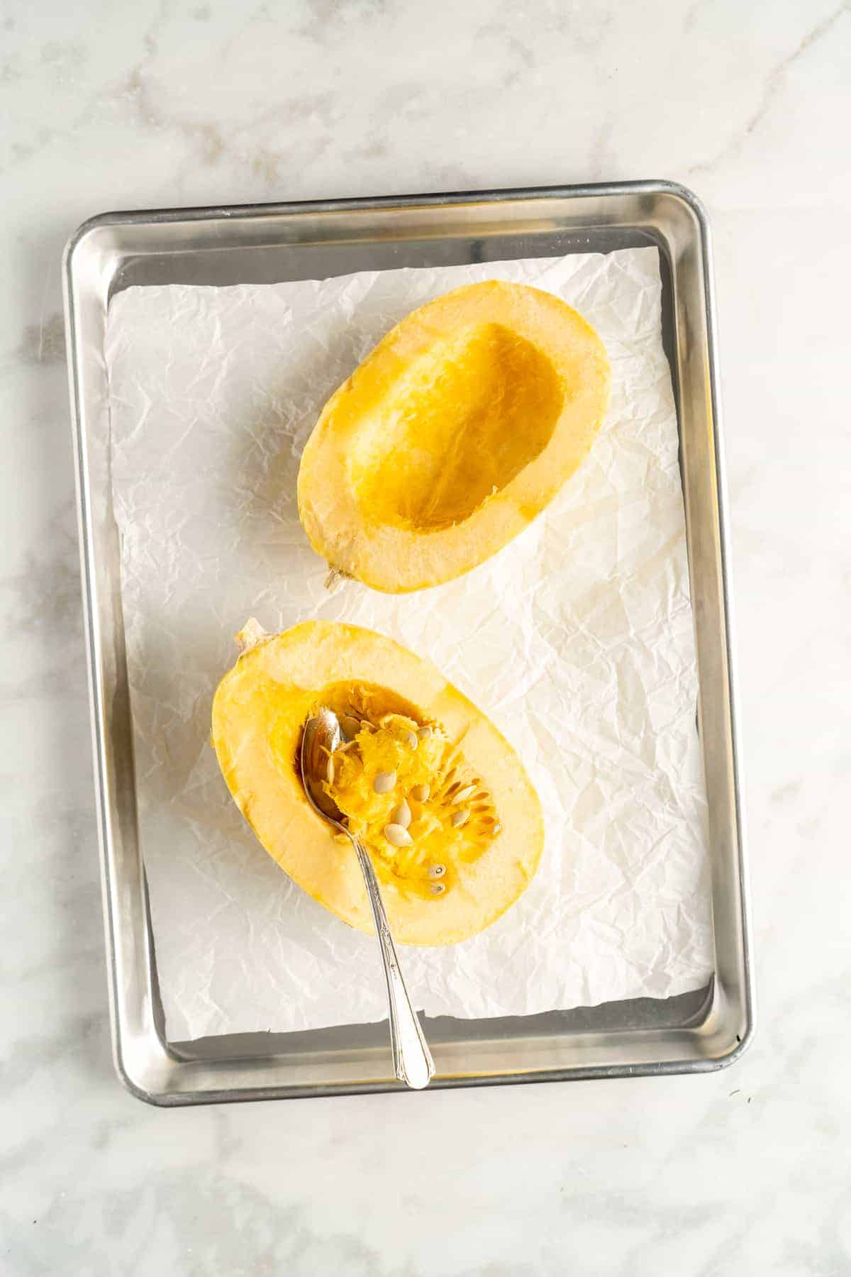 Overhead view of two spaghetti squash halves with spoon scooping out seeds