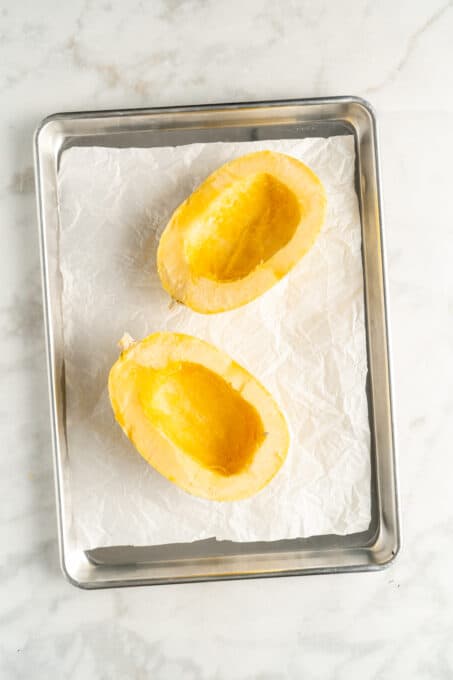 Overhead view of two spaghetti squash halves on parchment lined baking sheet
