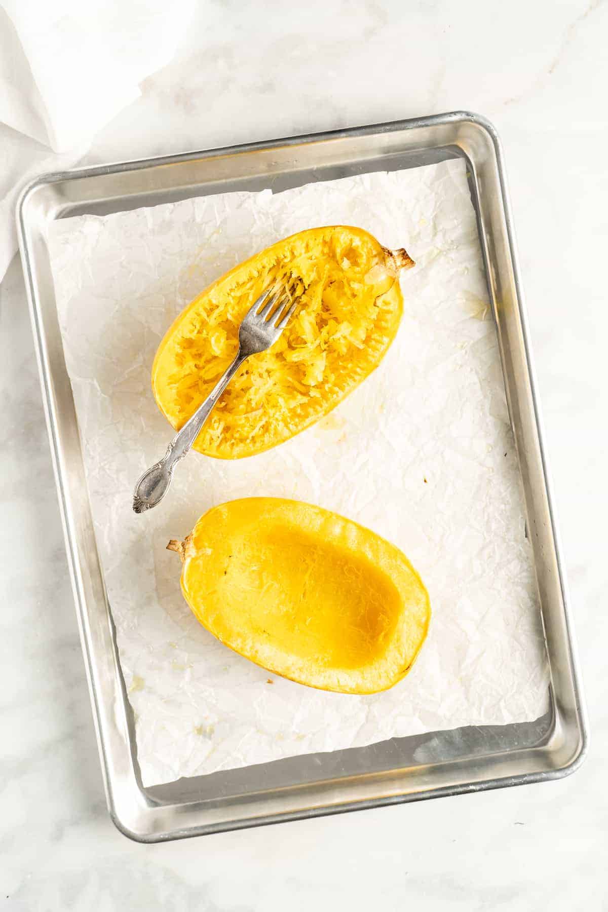 Overhead view of two spaghetti squash halves on parchment lined baking sheet with fork