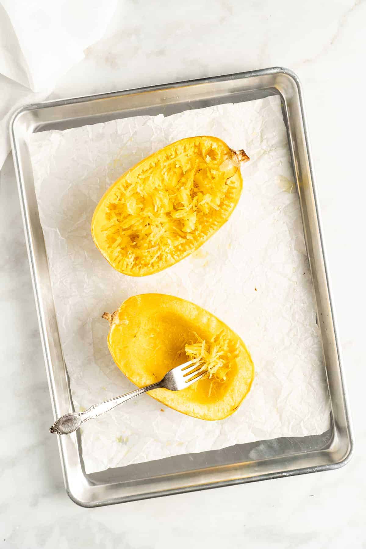 Overhead view of two spaghetti squash halves on baking sheet lined with parchment paper