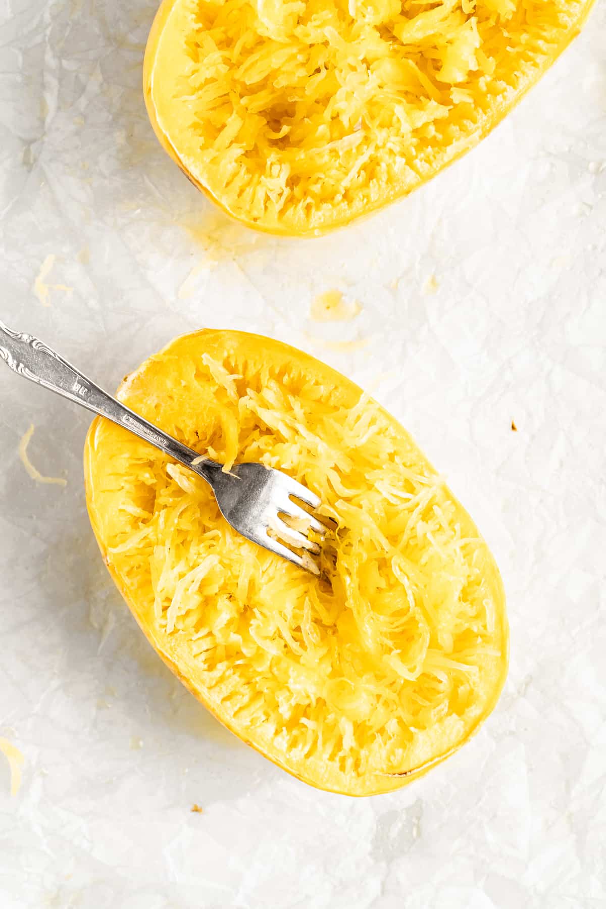 Two baked spaghetti squash halves with fork shredding flesh into noodles