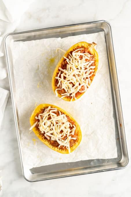 Overhead view of two spaghetti squash boats topped with cheese before baking