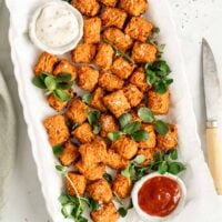 Overhead view of sweet potato tots on white platter with dipping sauces in bowls