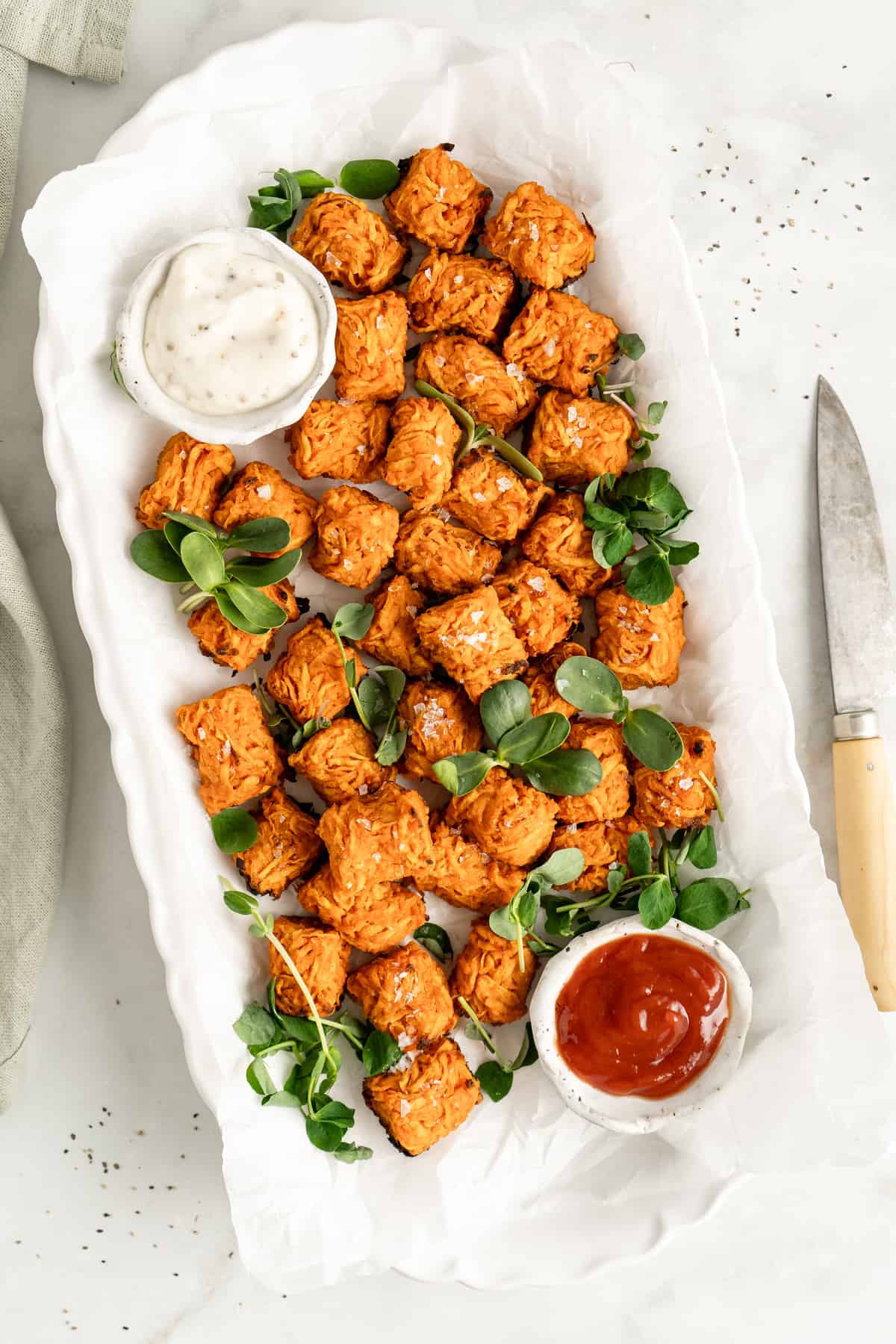 Overhead view of sweet potato tots on white platter with dipping sauces in bowls