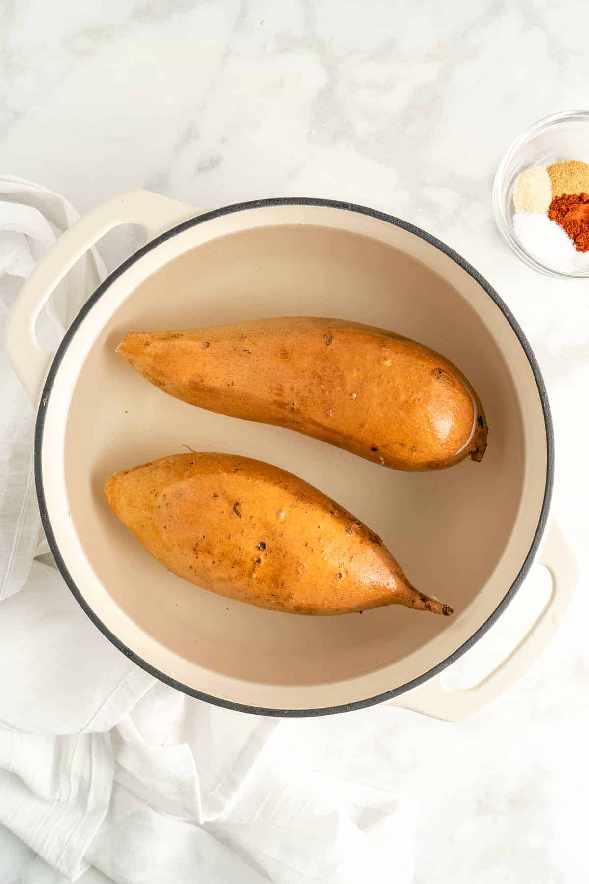 Overhead view of whole sweet potatoes being parboiled in pot