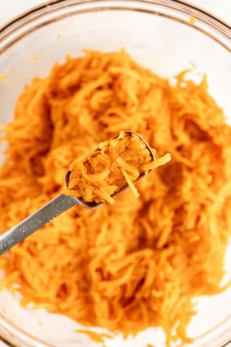 Shredded sweet potato mixture in measuring spoon above glass bowl