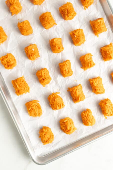 Overhead view of uncooked sweet potato tater tots on parchment lined baking sheet