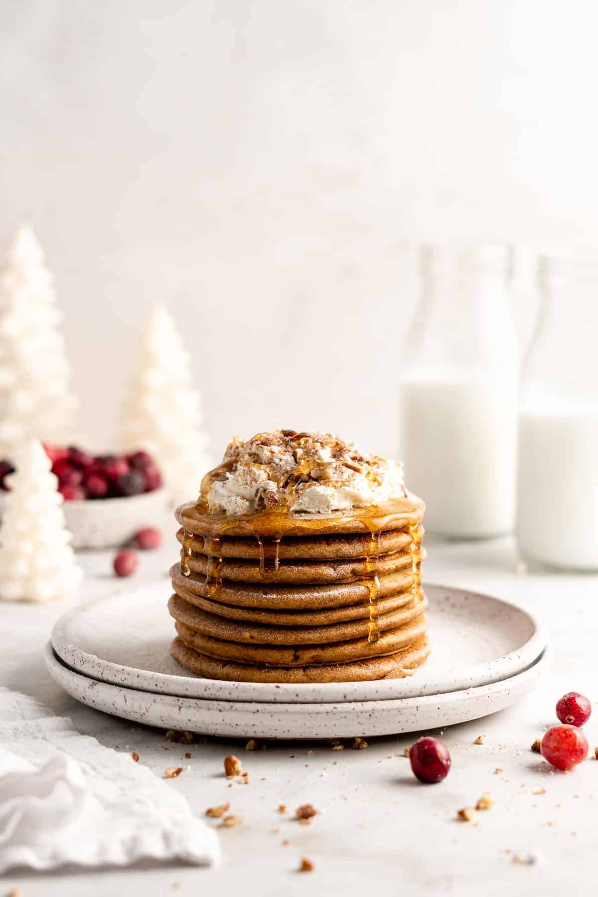 Stack of gingerbread pancakes topped with maple syrup, coconut cream, and nuts