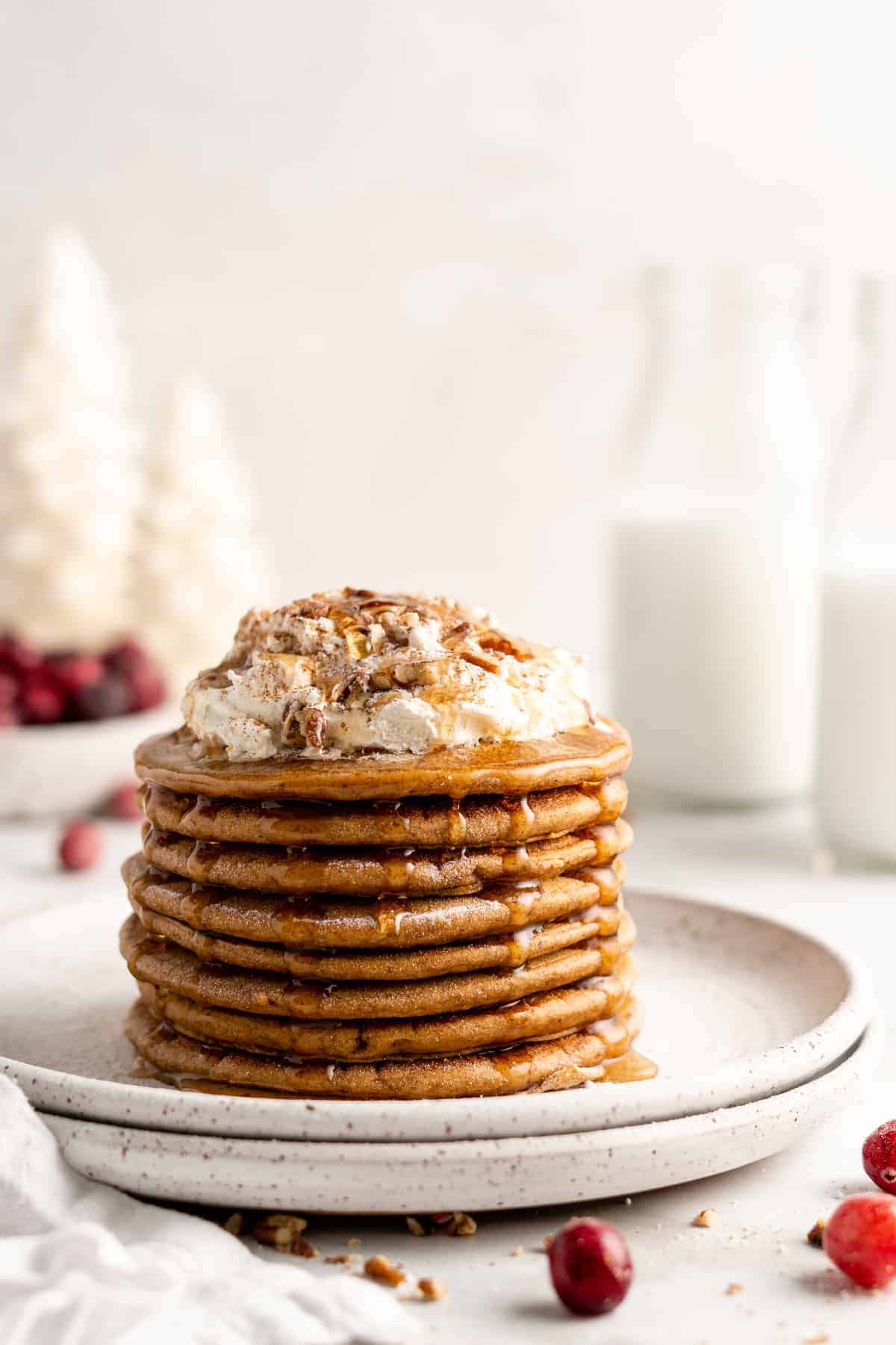 Stack of gingerbread pancakes topped with coconut whipped cream, nuts, and maple syrup