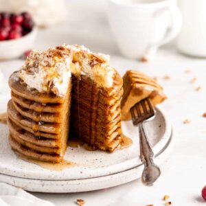 Stack of gingerbread pancakes topped with coconut whipped cream and maple syrup