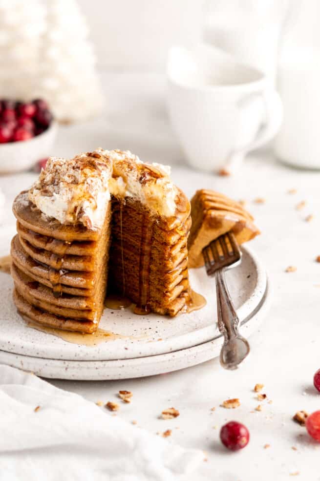 Stack of gingerbread pancakes topped with coconut whipped cream and maple syrup