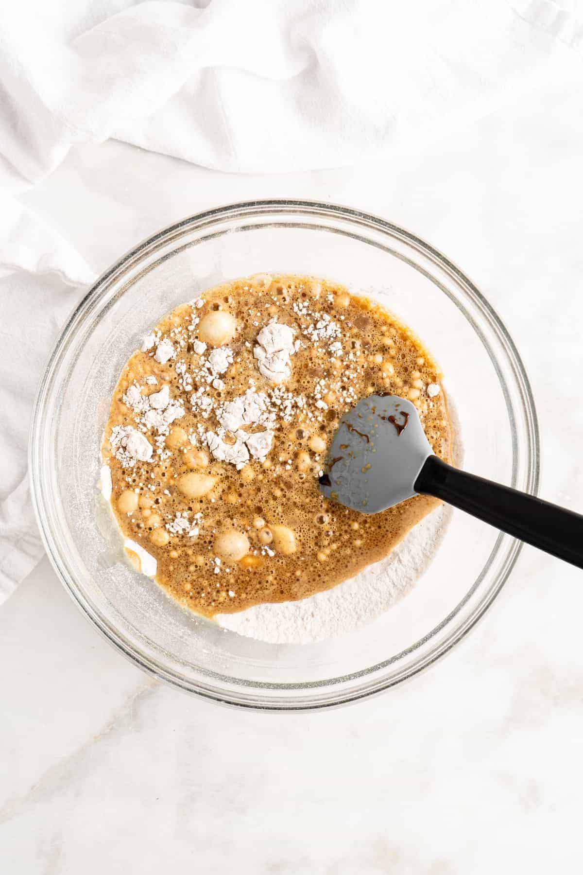 Black and gray spoon mixing pancake batter in glass bowl