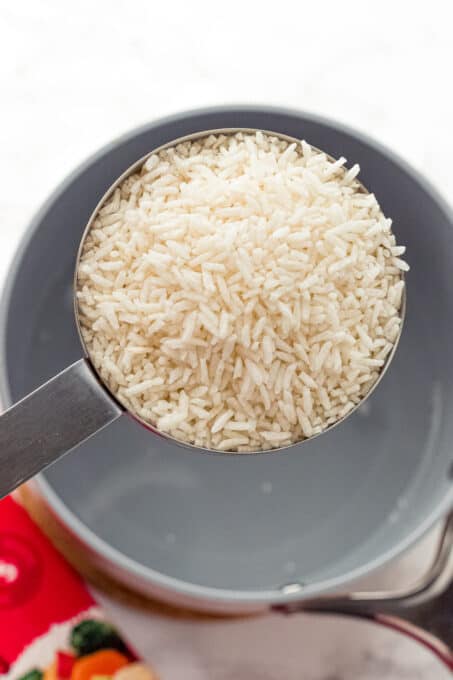 measuring cup filled with dry rice over boiling water