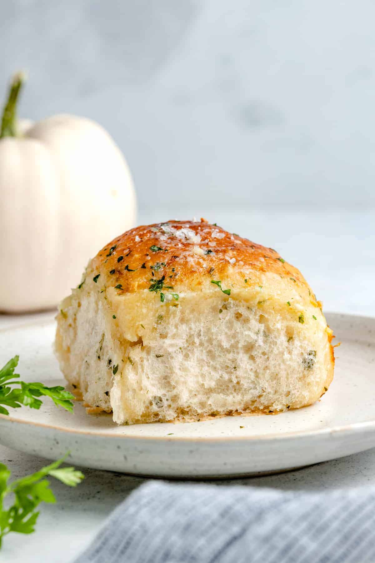 Single garlic dinner roll on a plate with a white pumpkin in the background