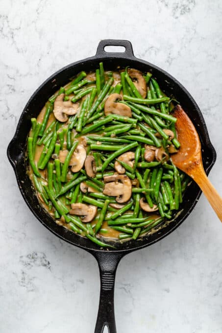 Overhead view of green beans and mushrooms in skillet with wooden spoon