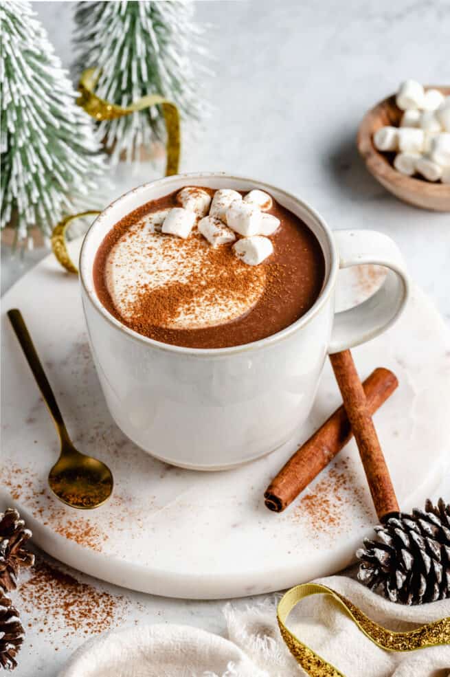 Mug of hot cocoa on round marble slab with spoon and cinnamon sticks