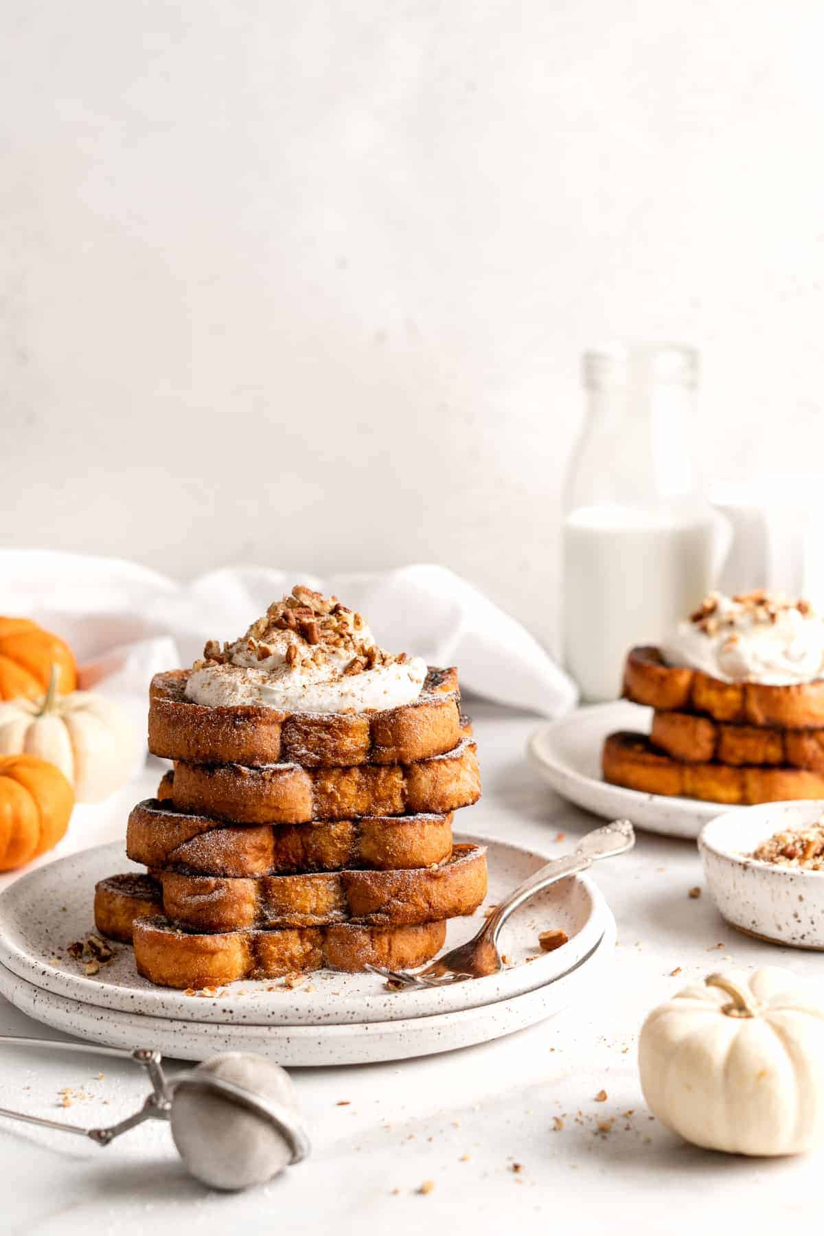 Two plates with stacks of pumpkin French toast topped with coconut whipped cream and nuts
