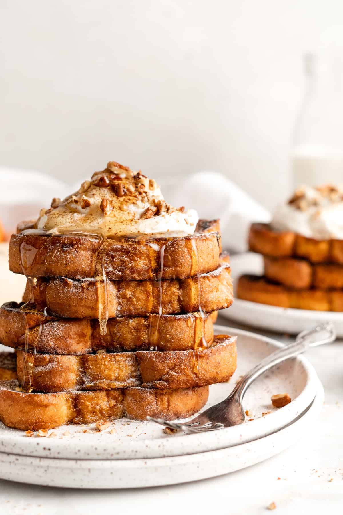 Two plates with stacks of pumpkin French toast topped with syrup, whipped cream, and nuts