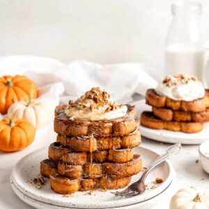 Two plates with stacks of pumpkin French toast garnished with whipped cream and nuts