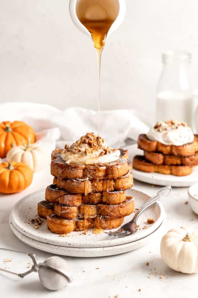 Pouring syrup over stack of pumpkin French toast topped with coconut cream and nuts