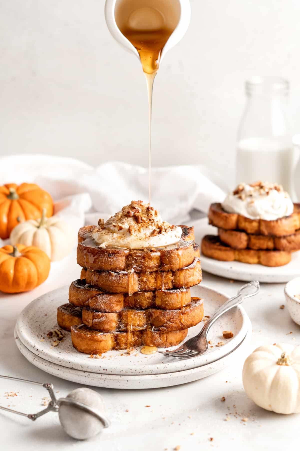 Pouring syrup over stack of pumpkin French toast topped with coconut cream and nuts