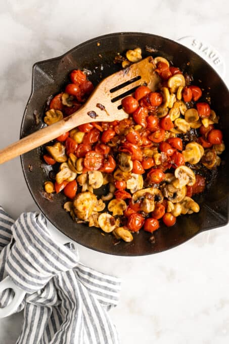 Overhead view of tomatoes and mushrooms being cooked in cast iron skillet
