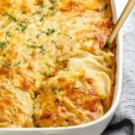 Vegan scalloped potatoes in baking dish with spoon scooping out a serving