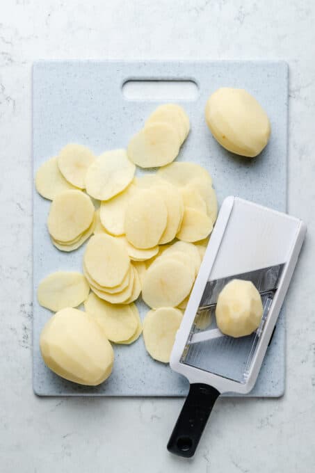 Overhead view of potatoes being sliced with mandoline slicer